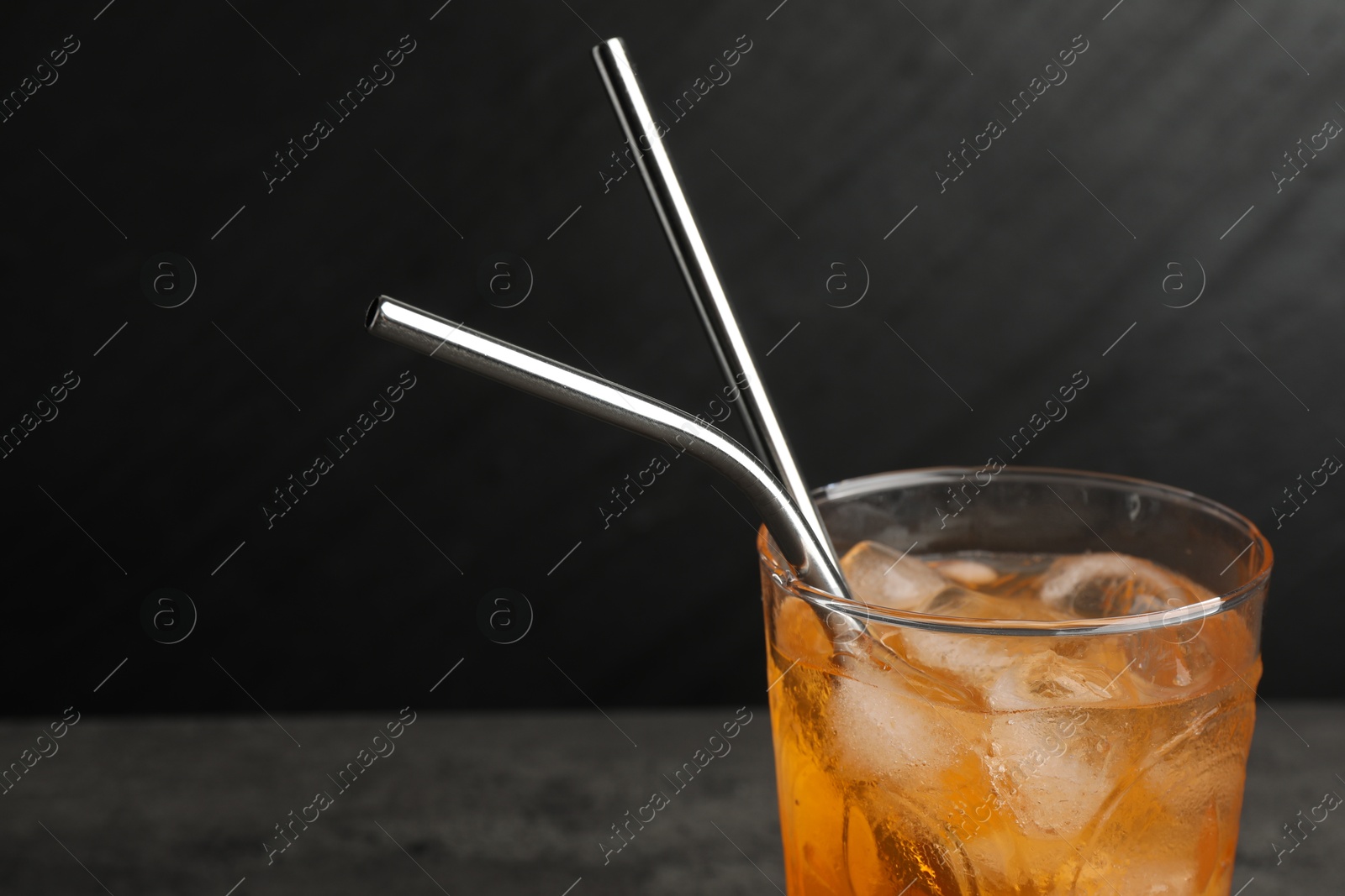 Photo of Tasty refreshing drink with straws in glass on dark background, closeup