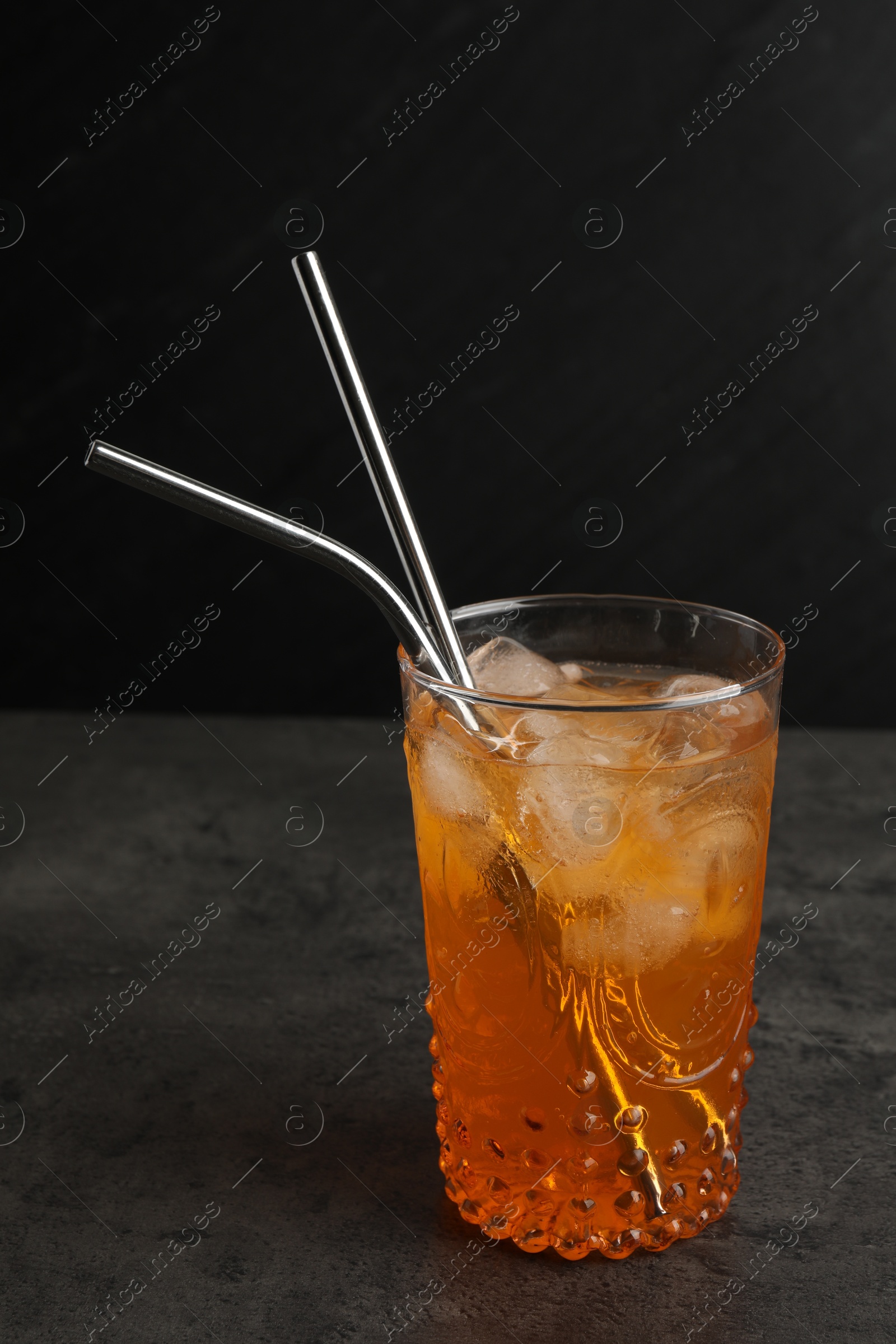 Photo of Tasty refreshing drink with straws in glass on grey textured table