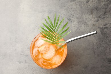 Photo of Tasty refreshing drink with straw and palm leaf in glass on grey table, top view