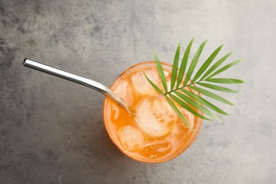 Photo of Tasty refreshing drink with straw and palm leaf in glass on grey table, top view