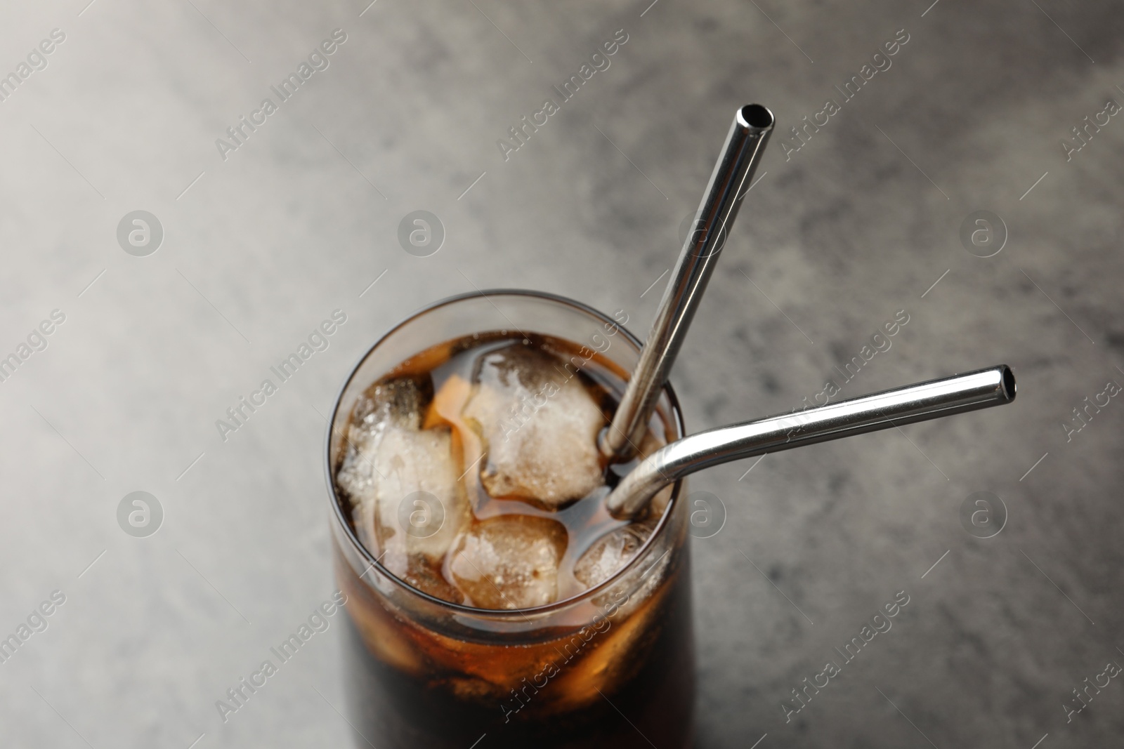 Photo of Tasty refreshing drink with straws in glass on grey table, closeup