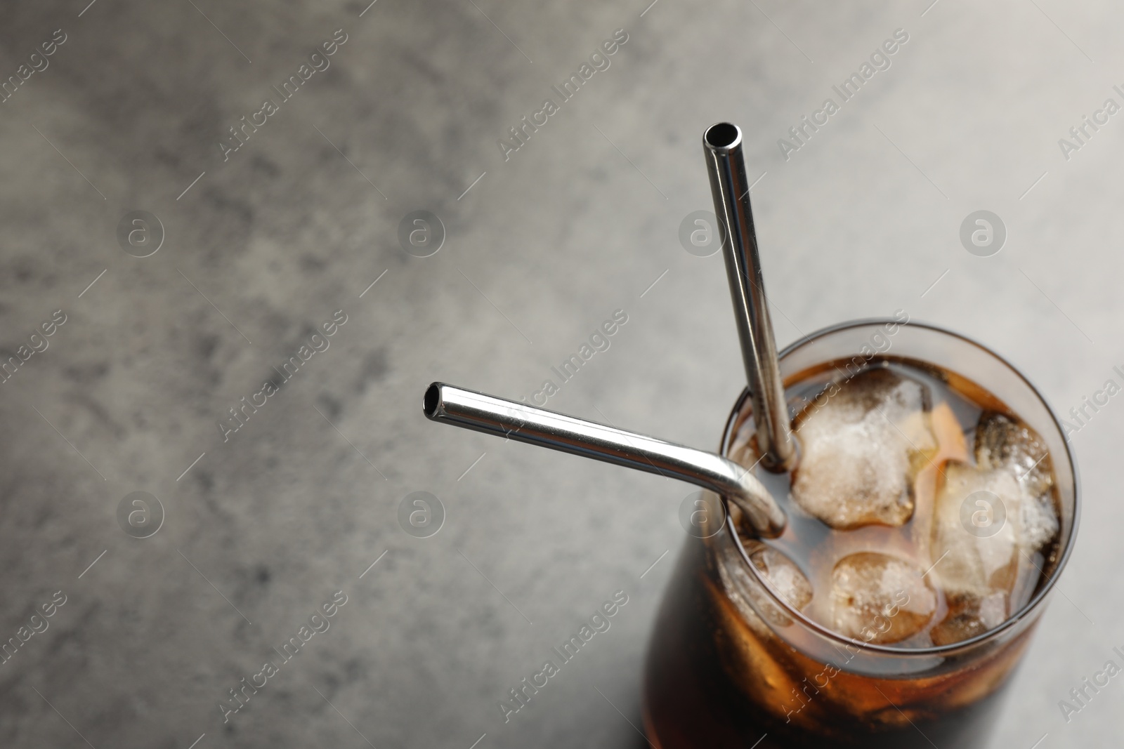 Photo of Tasty refreshing drink with straws in glass on grey table, closeup. Space for text