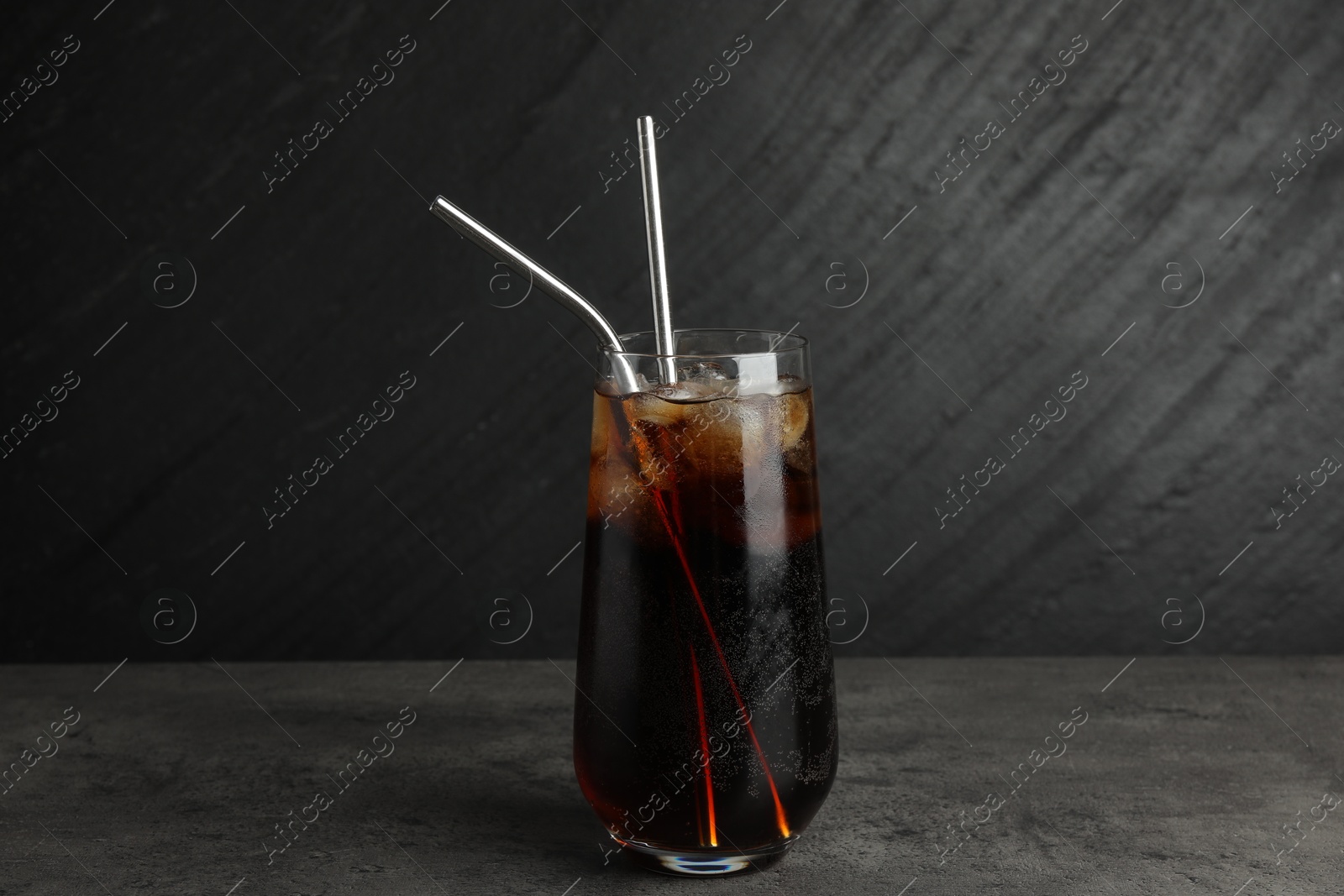 Photo of Tasty refreshing drink with straws in glass on grey textured table