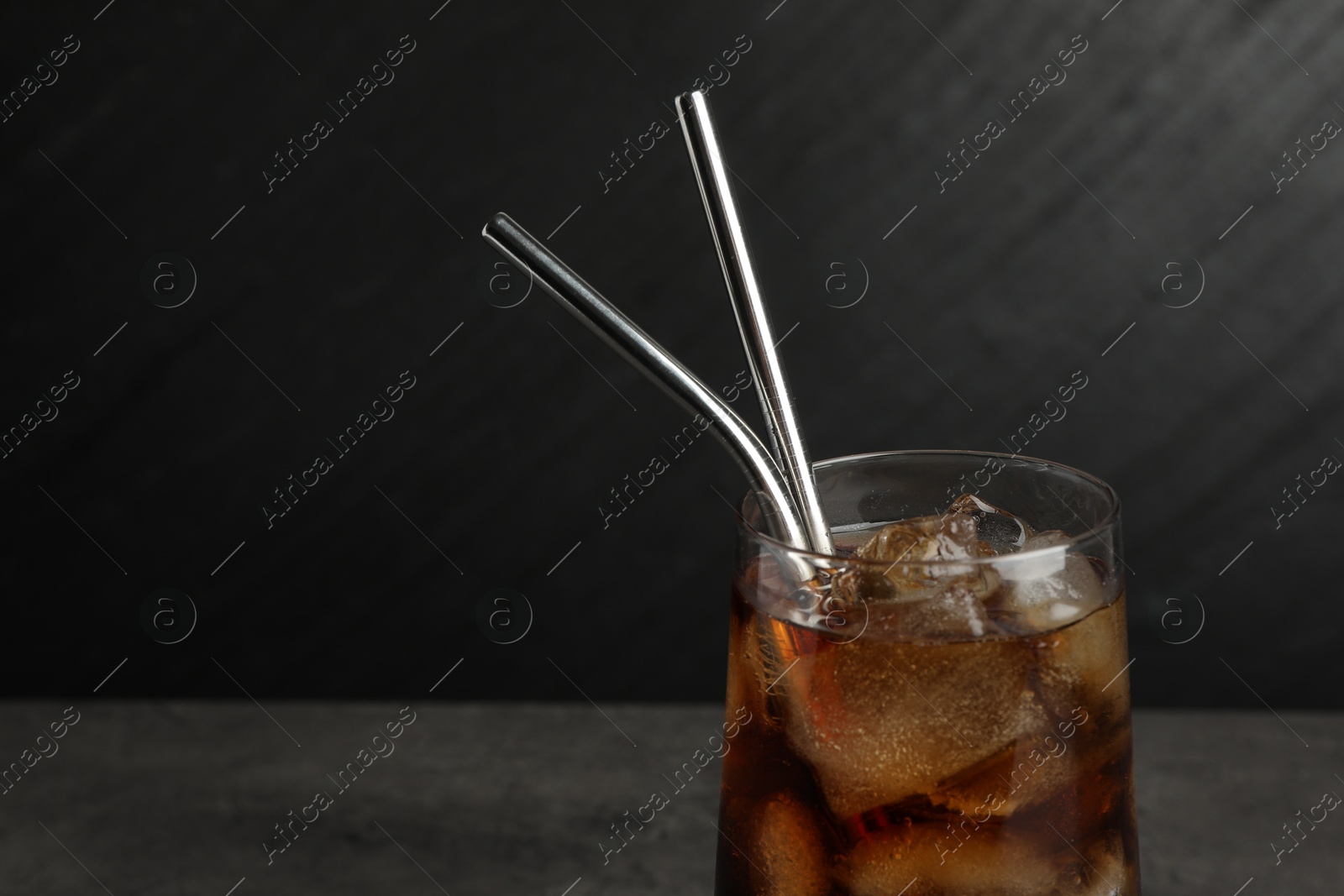 Photo of Tasty refreshing drink with straws in glass on dark background, closeup