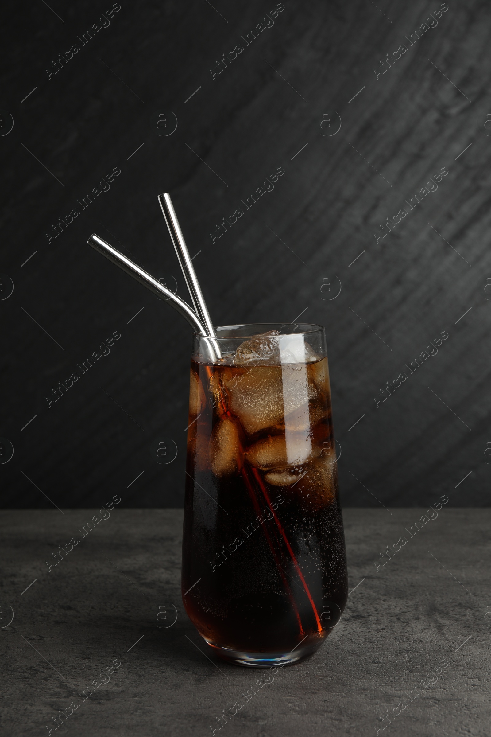 Photo of Tasty refreshing drink with straws in glass on grey textured table