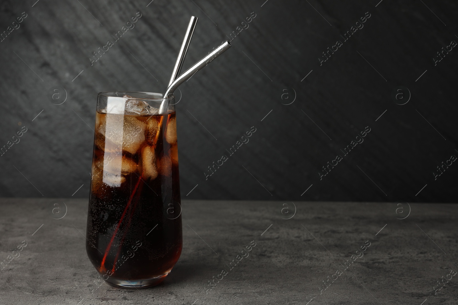 Photo of Tasty refreshing drink with straws in glass on grey textured table, space for text