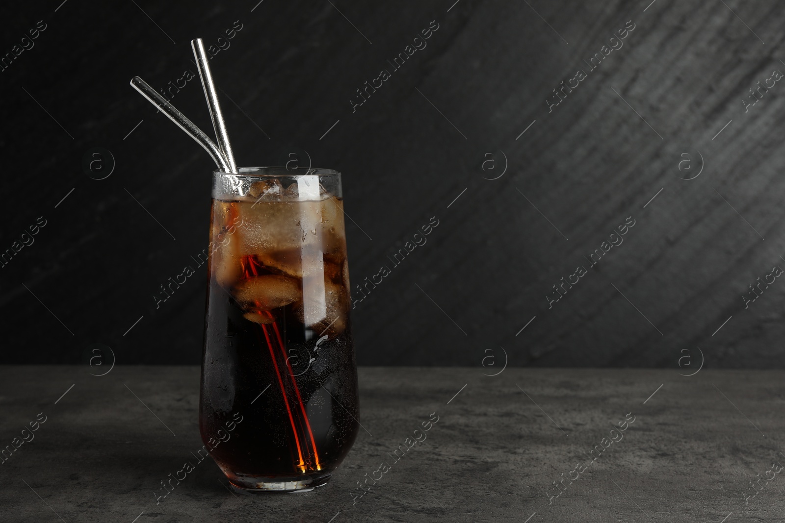 Photo of Tasty refreshing drink with straws in glass on grey textured table, space for text