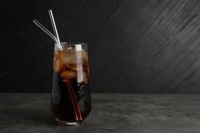 Photo of Tasty refreshing drink with straws in glass on grey textured table, space for text