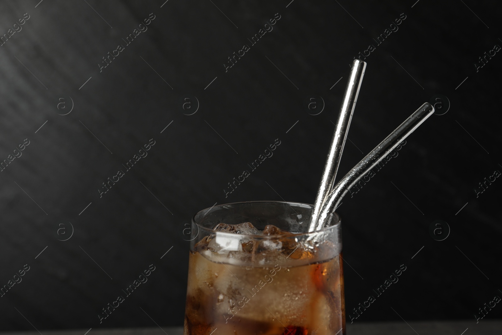 Photo of Tasty refreshing drink with straws in glass on dark background, closeup