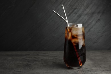 Tasty refreshing drink with straws in glass on grey textured table, space for text