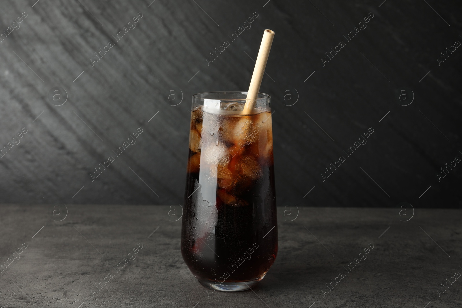 Photo of Tasty refreshing drink with straw in glass on grey textured table