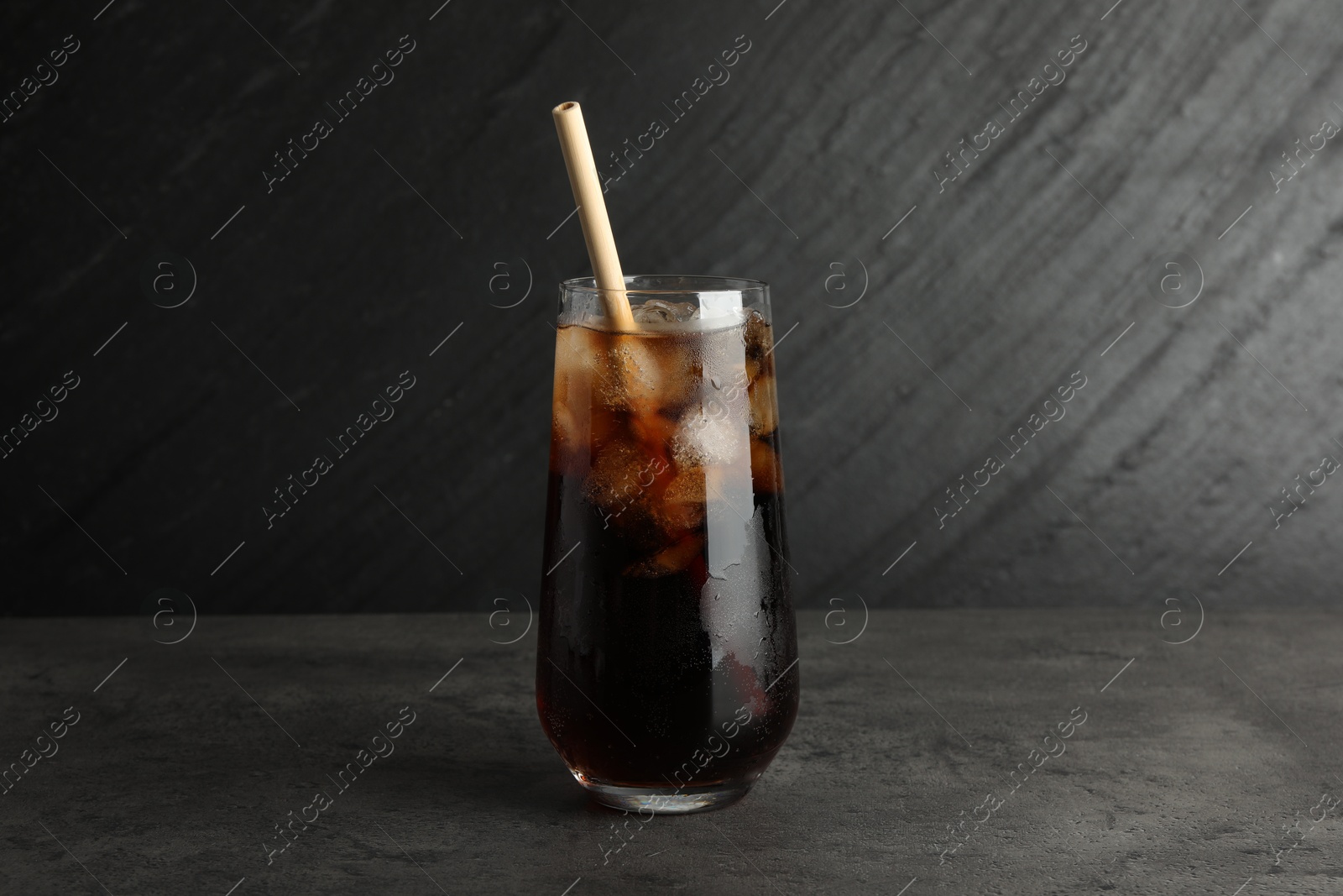 Photo of Tasty refreshing drink with straw in glass on grey textured table