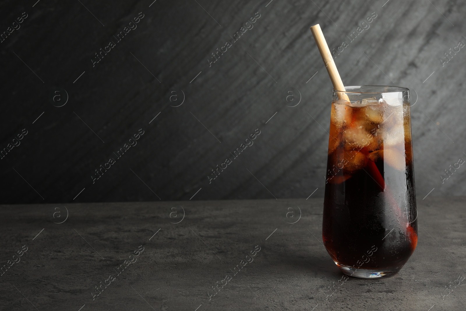 Photo of Tasty refreshing drink with straw in glass on grey textured table, space for text