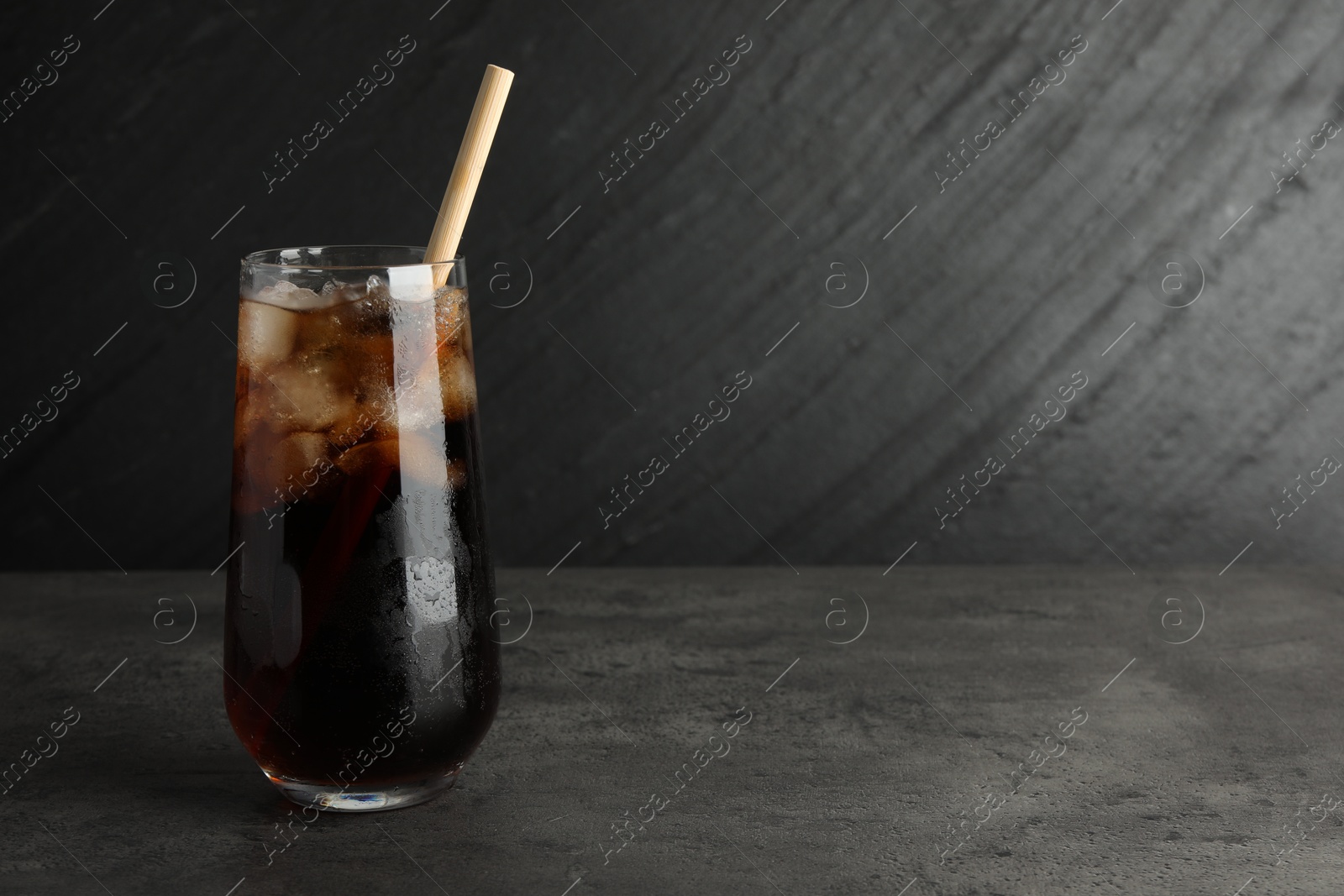 Photo of Tasty refreshing drink with straw in glass on grey textured table, space for text