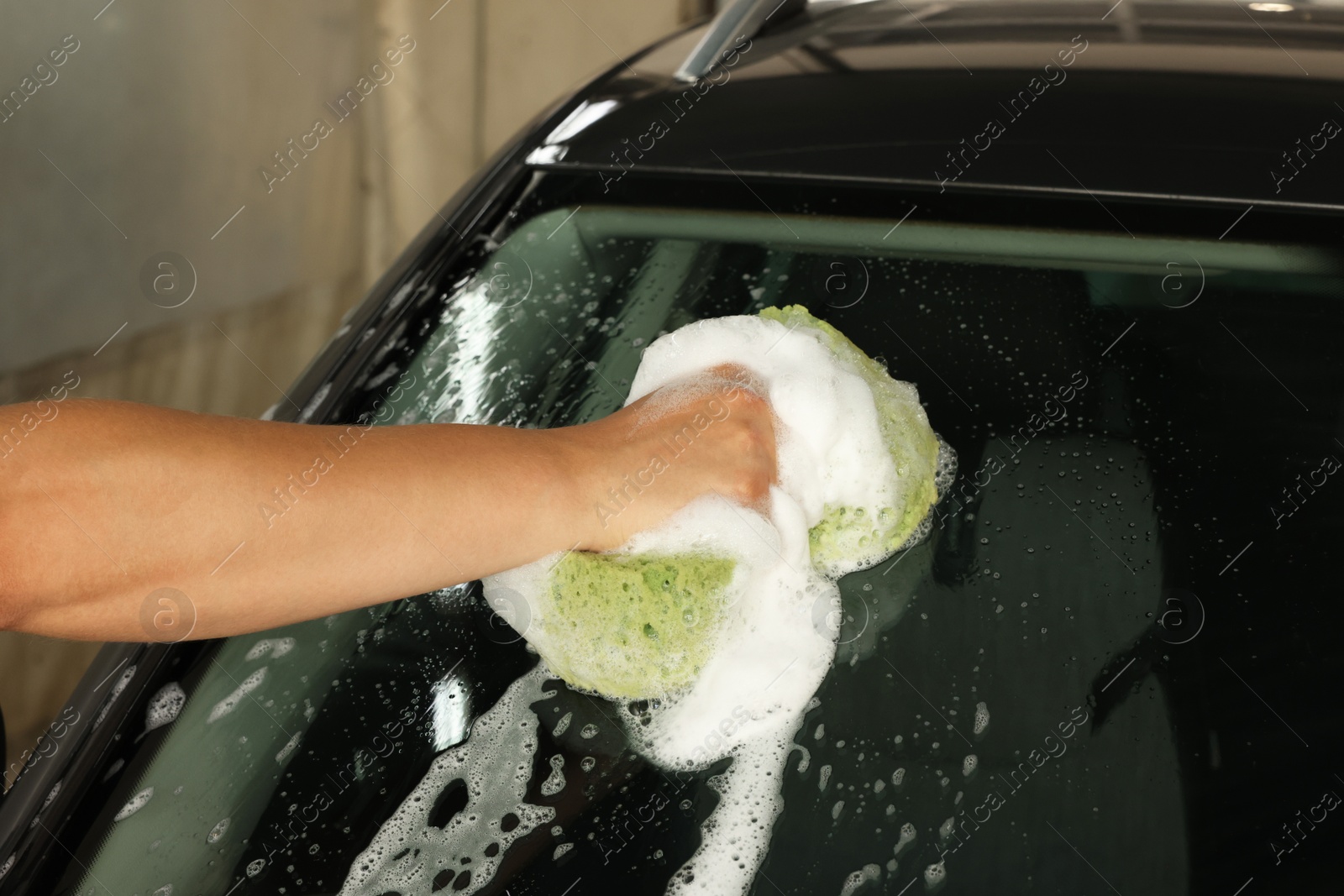 Photo of Man washing car windshield with sponge indoors, closeup