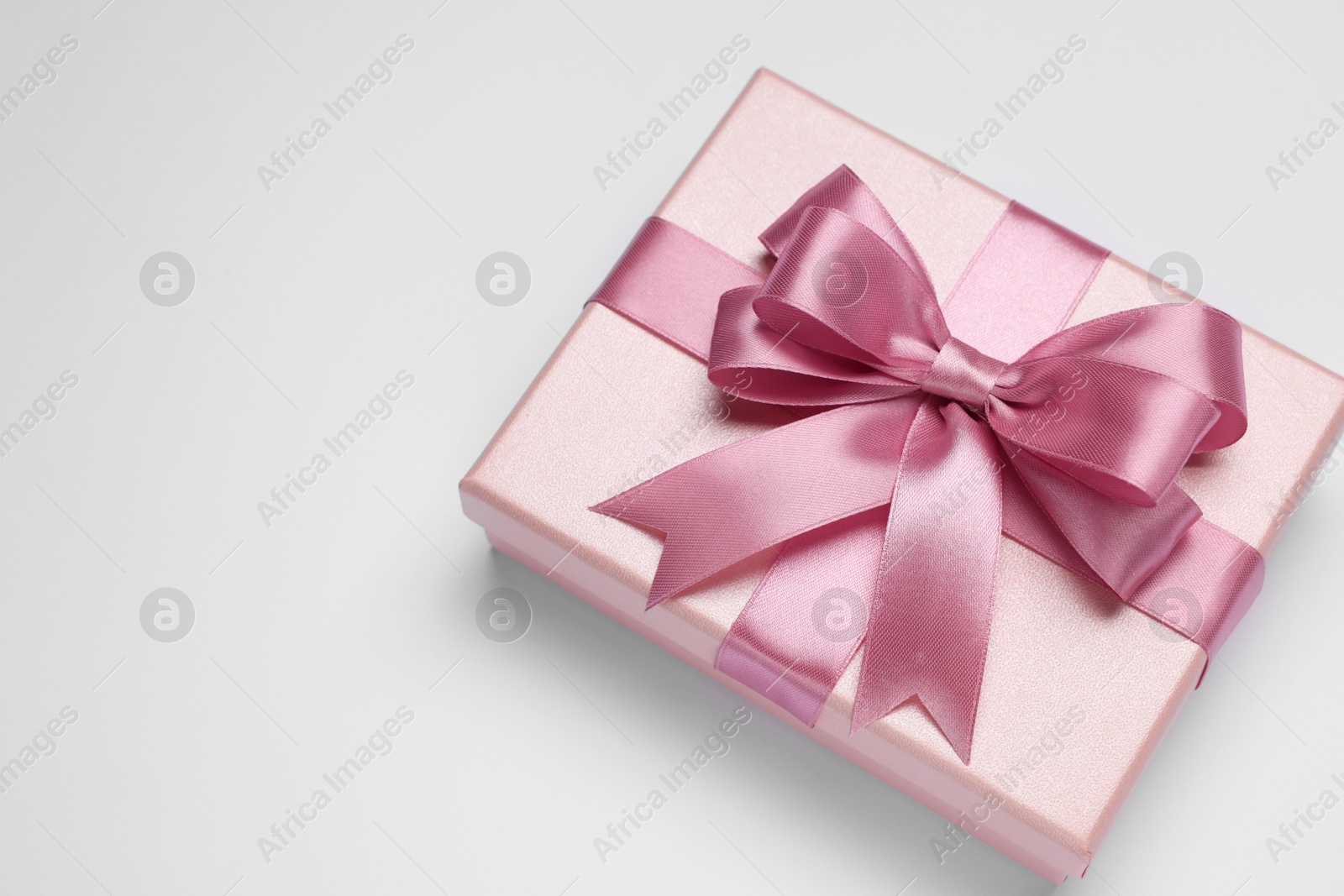 Photo of Gift box with pink bow on light grey background, top view. Space for text