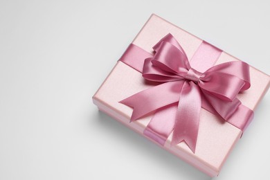 Gift box with pink bow on light grey background, top view. Space for text