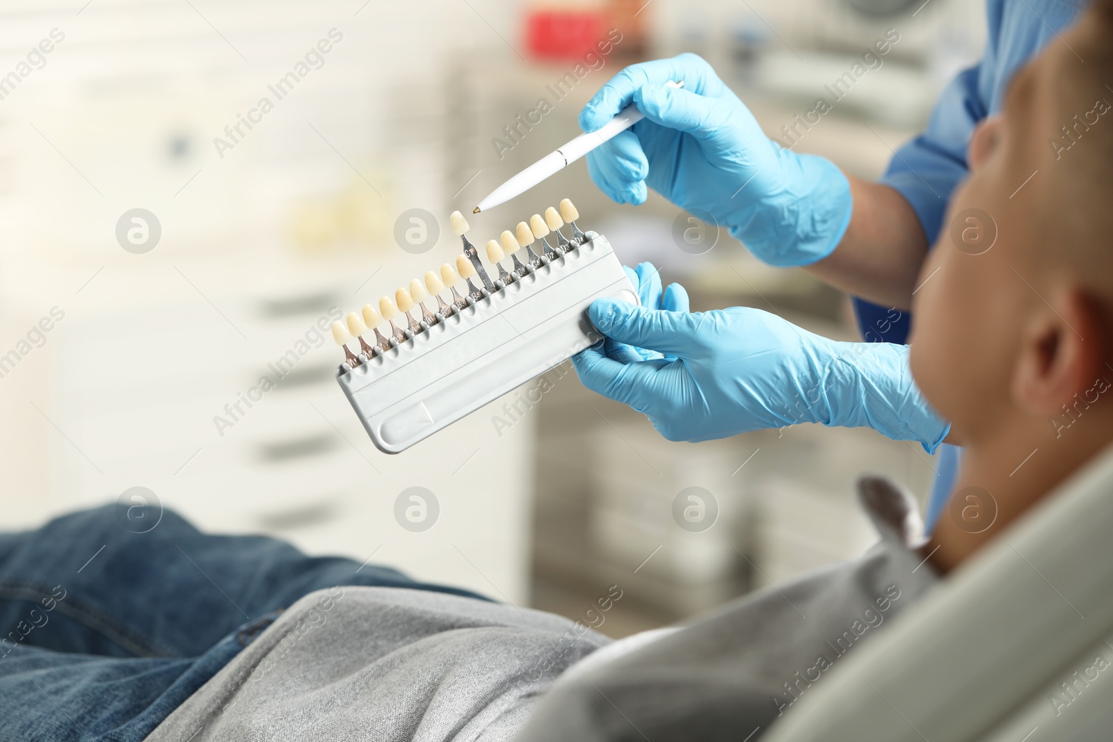 Photo of Doctor and patient choosing shade on teeth color palette in clinic, closeup. Dental veneers