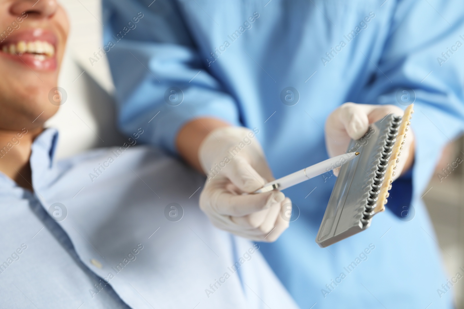 Photo of Doctor and patient choosing shade on teeth color palette in clinic, closeup. Dental veneers