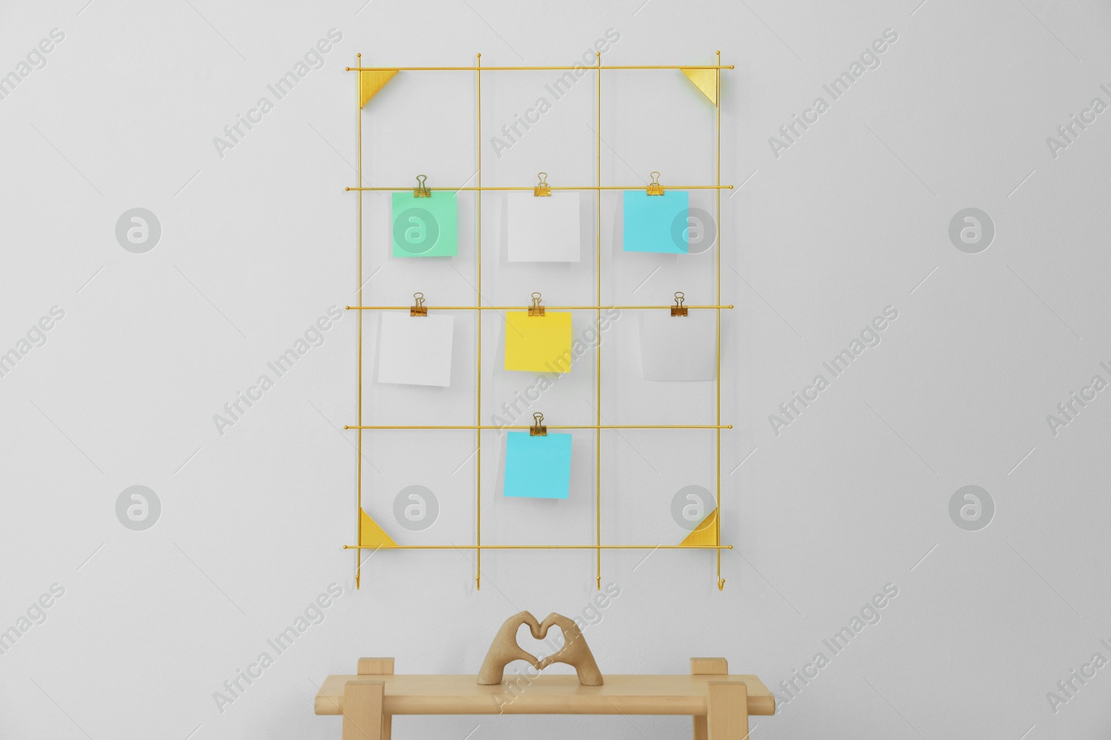 Photo of Mood board with blank paper notes and decorative figure in shape of hands making heart on wooden ladder near white wall