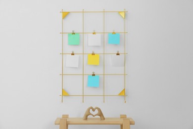 Photo of Mood board with blank paper notes and decorative figure in shape of hands making heart on wooden ladder near white wall