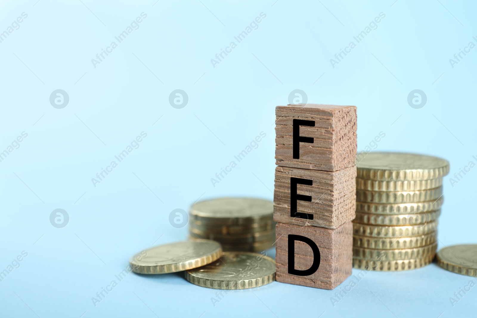 Photo of Stack of wooden cubes with letters Fed (Federal Reserve System) and coins on light blue background, closeup. Space for text