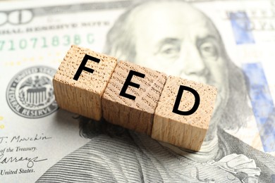 Photo of Wooden cubes with letters Fed (Federal Reserve System) on dollar banknote, closeup