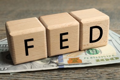 Photo of Wooden cubes with letters Fed (Federal Reserve System) and dollar banknotes on table, closeup