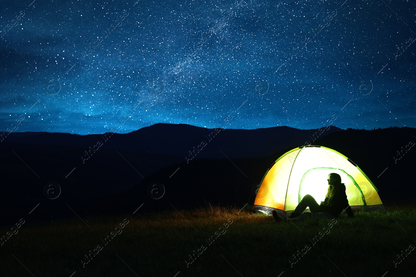 Photo of Woman sitting near modern camping tent in wilderness at night, space for text