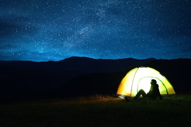 Photo of Woman sitting near modern camping tent in wilderness at night, space for text