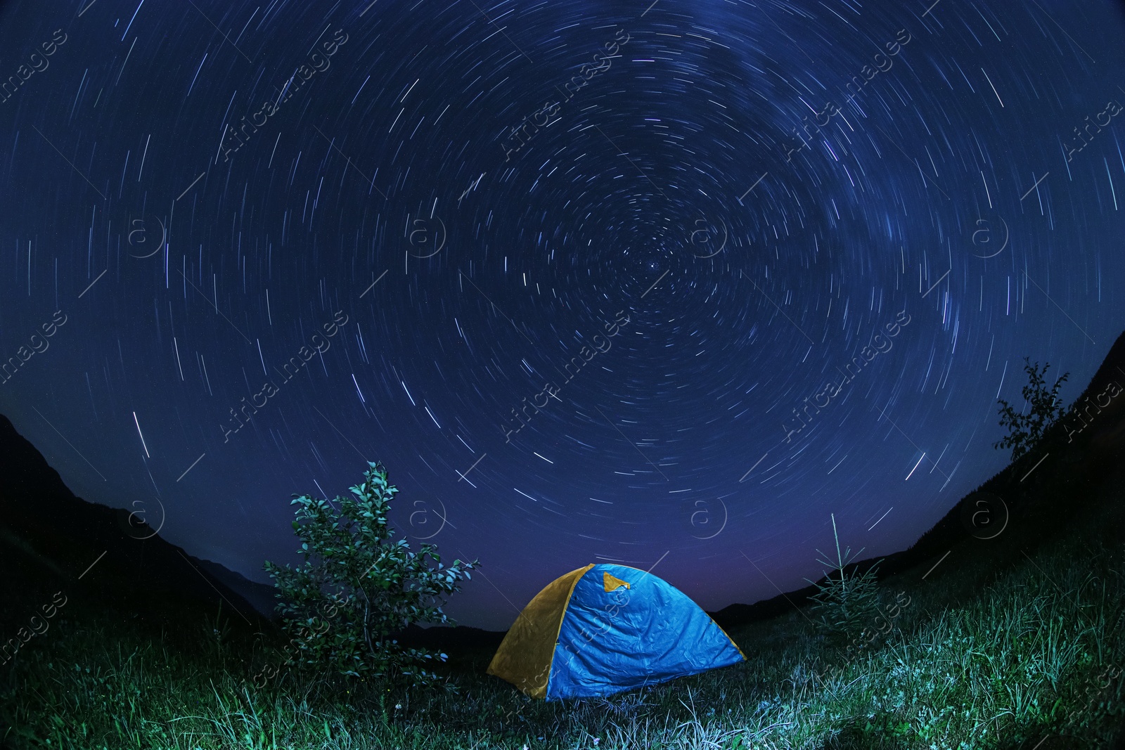 Photo of Modern camping tent in wilderness at night. Fisheye lens effect