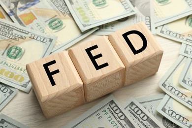 Photo of Cubes with letters Fed (Federal Reserve System) and dollar banknotes on white wooden table, closeup