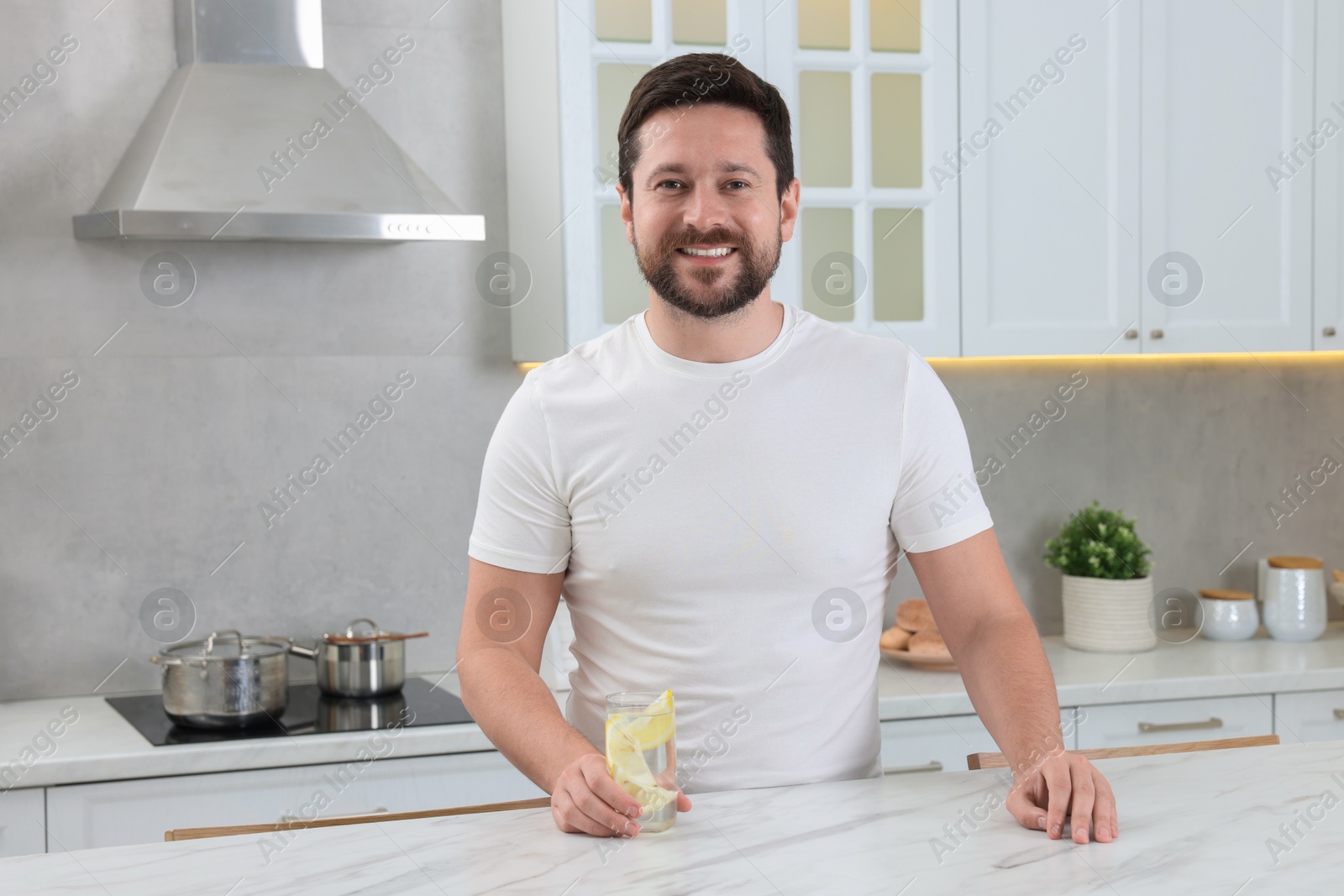 Photo of Happy man holding glass of water with lemon in kitchen