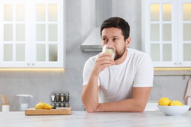 Photo of Handsome man drinking water with lemon in kitchen