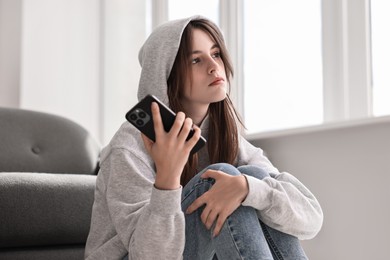 Loneliness concept. Sad teenage girl with smartphone listening to voice message at home