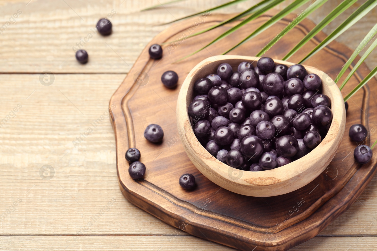 Photo of Ripe acai berries in bowl and palm leaves on wooden table. Space for text