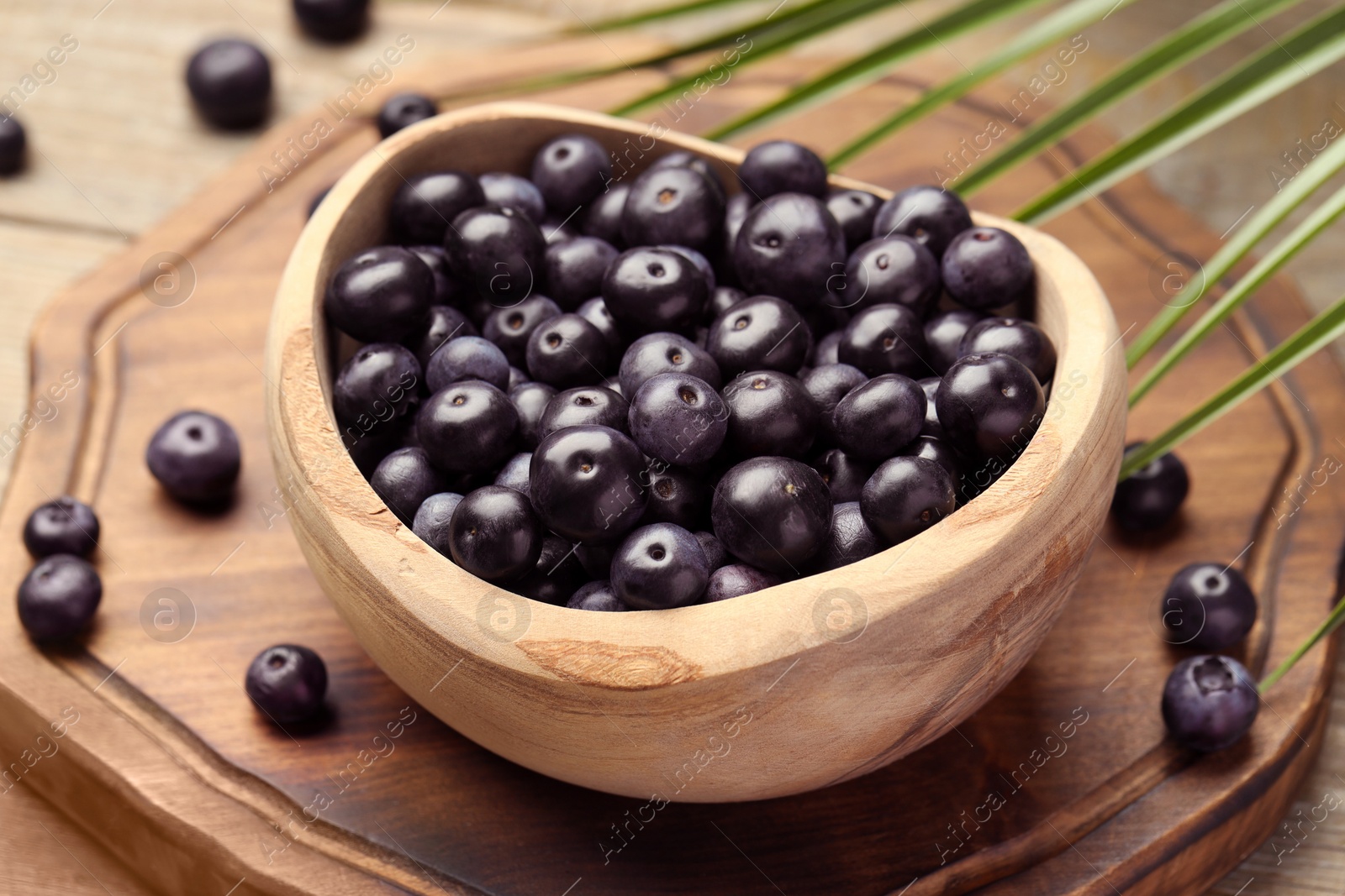 Photo of Ripe acai berries in bowl and palm leaves on wooden table, closeup