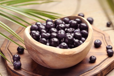 Photo of Ripe acai berries in bowl and palm leaves on wooden table, closeup