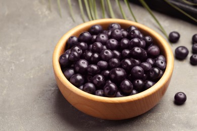 Ripe acai berries in bowl on grey textured table, closeup