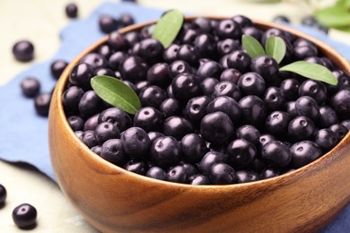 Photo of Ripe acai berries and leaves in bowl on grey table, closeup