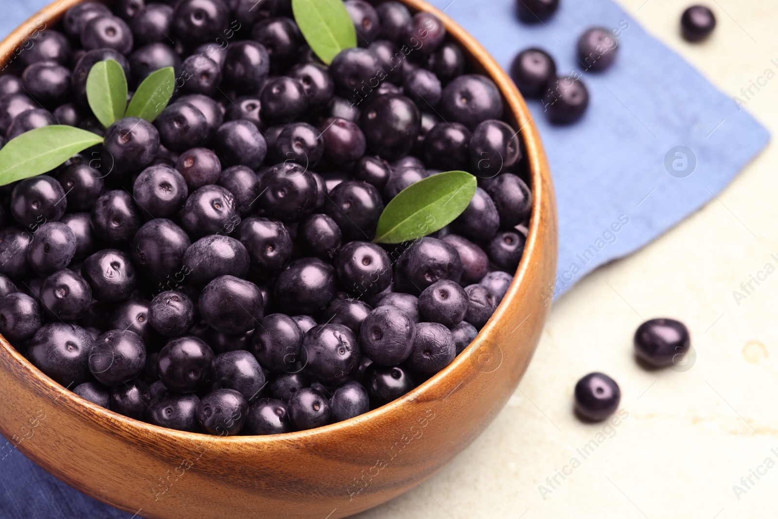 Photo of Ripe acai berries and leaves in bowl on grey table, closeup