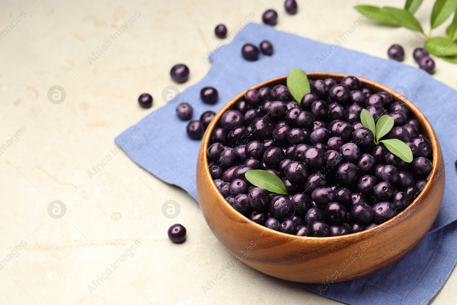 Photo of Ripe acai berries and leaves in bowl on grey table. Space for text