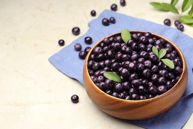 Photo of Ripe acai berries and leaves in bowl on grey table. Space for text