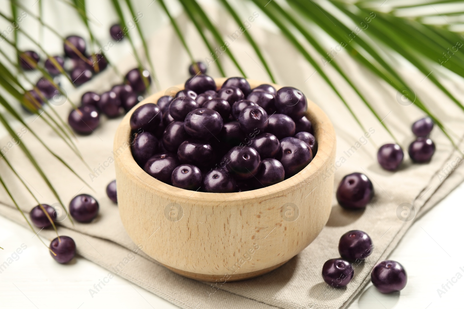 Photo of Ripe acai berries in bowl on light table, closeup