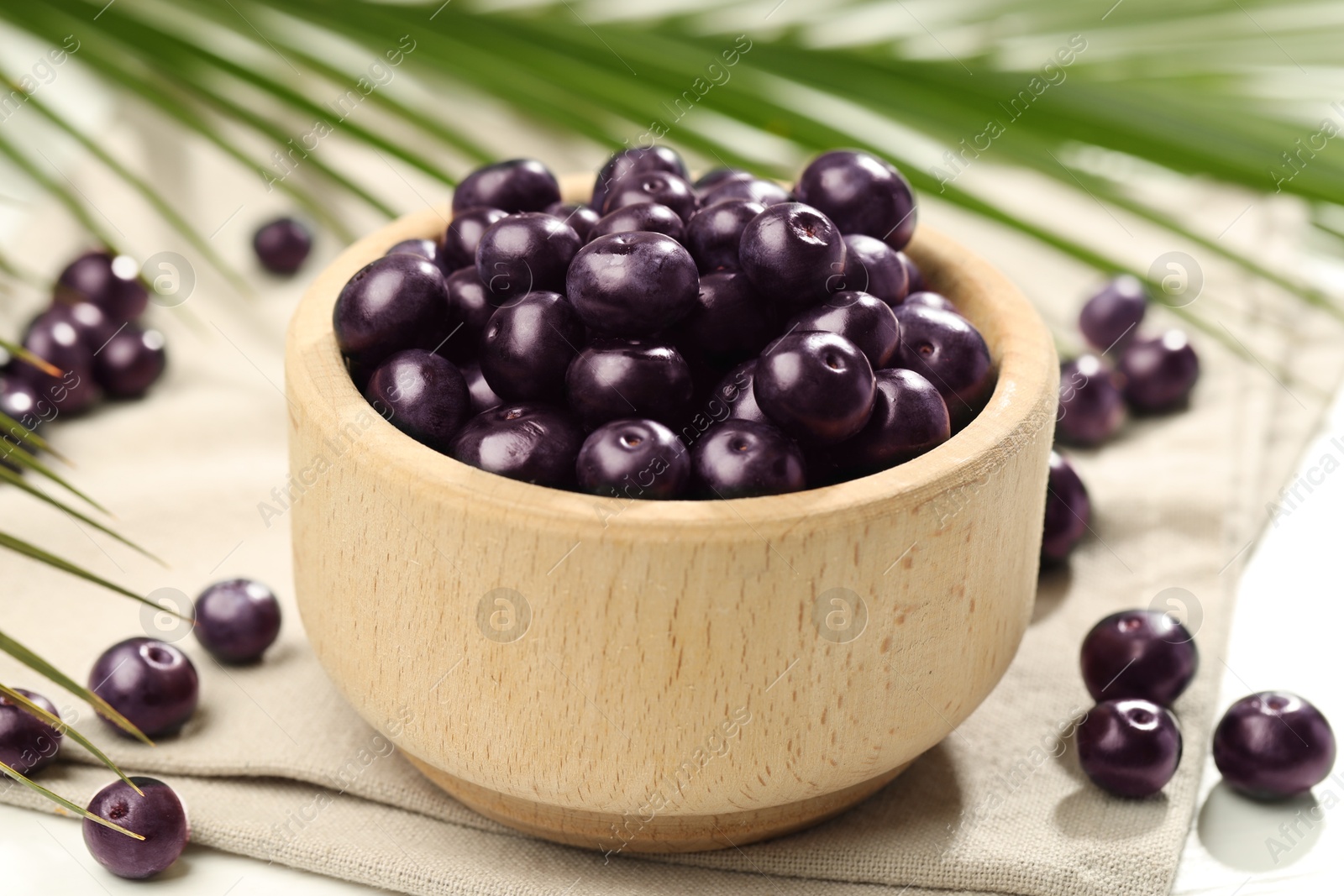 Photo of Ripe acai berries in bowl on light table, closeup