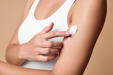 Woman applying cream onto arm against beige background, closeup. Body care