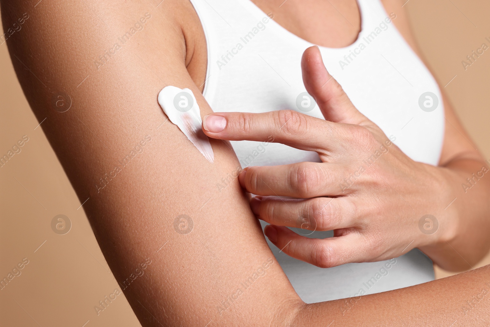 Photo of Woman applying cream onto arm against beige background, closeup. Body care