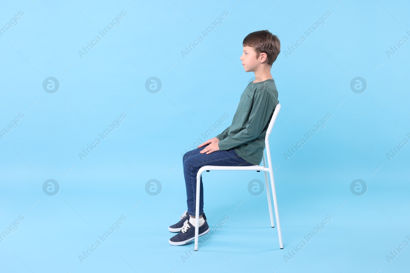 Photo of Boy with correct posture sitting on chair against light blue background