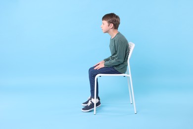 Photo of Boy with incorrect posture sitting on chair against light blue background