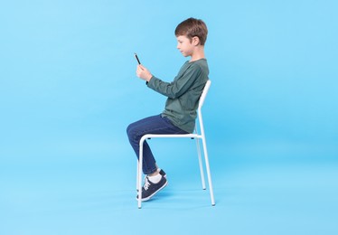 Photo of Boy with correct posture and phone sitting on chair against light blue background